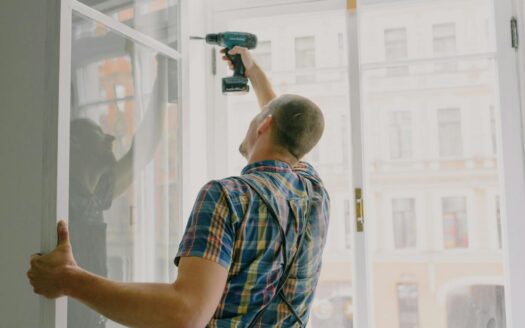 Back view of worker in checkered shirt drilling window frame during renovation process in apartment