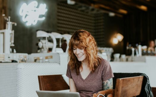 woman sitting on brown wooden chair while using silver laptop computer in room