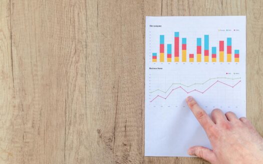 Hand analyzing business graphs on a wooden desk, focusing on data results and growth analysis.